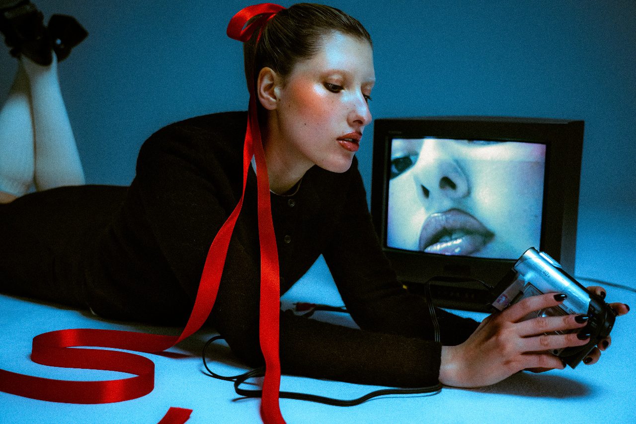 A woman lying on the floor holding a camcorder beside a television